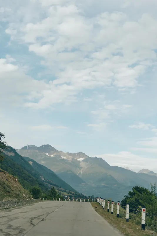 Scenic mountain road winding through rugged hills under a bright blue sky, guardrails along the asphalt, capturing an expansive outdoor landscape and tranquil travel atmosphere.