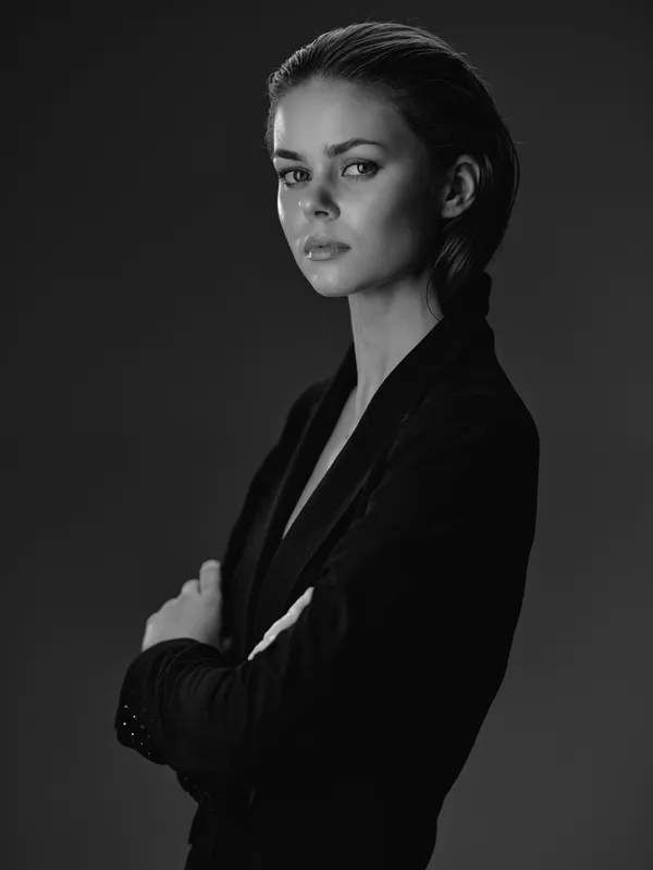 Black and white portrait of a serious woman in a blazer with crossed arms, showcasing confidence and elegance in studio lighting.