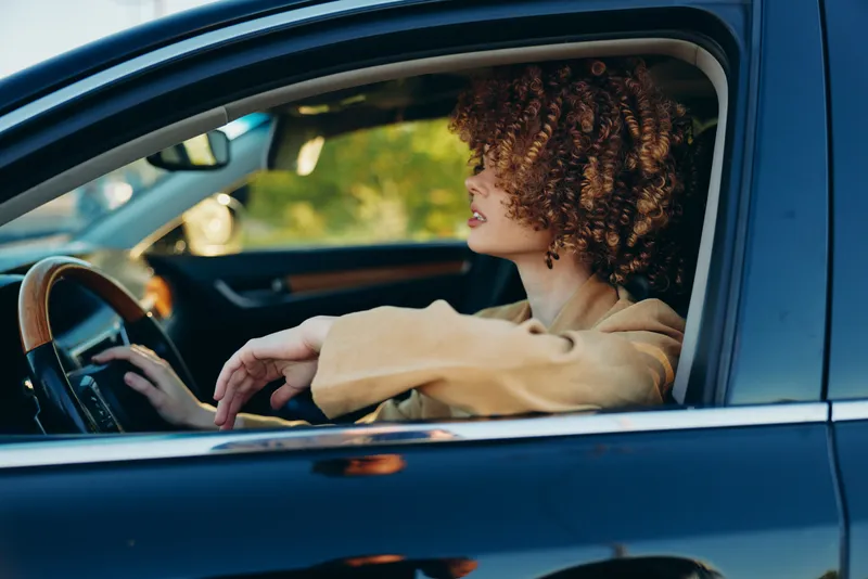 Casual woman driver sits in a car, enjoying a relaxed lifestyle moment, retro film color tones, warm natural light through the window, candid portrait inside a moving vehicle