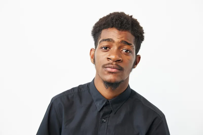 A thoughtful black man wearing a black shirt, showing a serious expression in a minimalist setting. This image captures depth and introspection effectively.