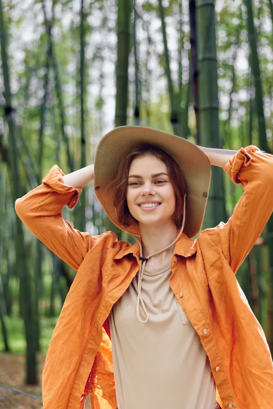 Woman portrait smile hat bamboo forest outdoors nature, happy young woman wearing wide brim hat and orange jacket standing in bamboo grove, relaxed lifestyle and travel portrait.