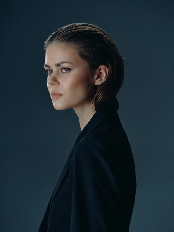 Serious woman with dark hair in black jacket on dark background, contemplative expression, studio portrait, moody lighting