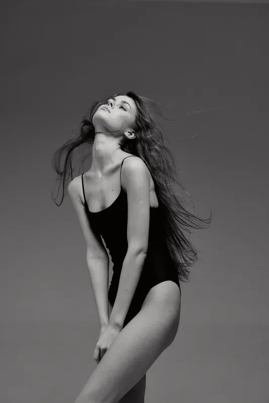 Black and white portrait of a slim woman in a black bodysuit posing with flowing hair and serene expression.