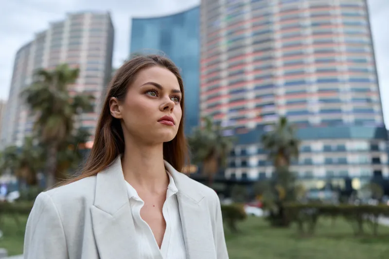 Woman confident in white blazer with urban background, thoughtful expression, modern business style, natural daylight, spring season, professional business woman