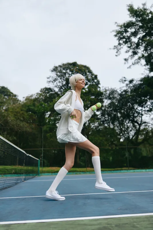 Young athletic woman enjoying a game of tennis outdoors, wearing sporty attire with a cheerful expression on a green court surrounded by trees