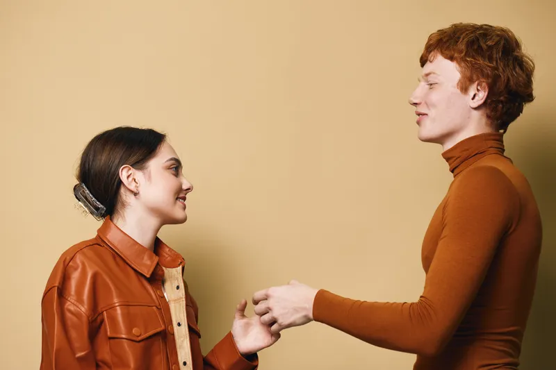 Young man and woman shaking hands against beige background with casual clothing smiling and making connection for friendship or greeting in studio. Interaction, communication and people.