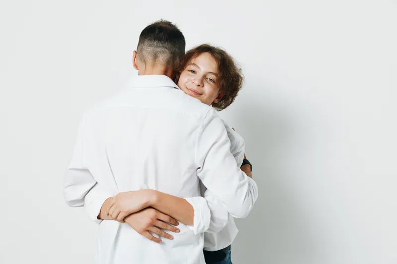 A professional man in business attire shares a warm moment with a colleague, showcasing confidence and care against an isolated colored backdrop.