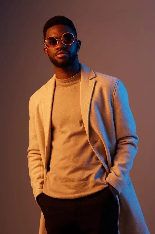Stylish young African man in sunglasses posing confidently against a gradient background, showcasing modern fashion and urban lifestyle concepts