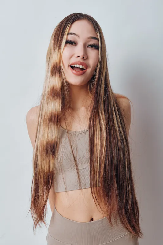 Young woman with long straight hair and casual outfit smiling and posing indoors on plain background. Beauty, fashion and natural look for lifestyle portrait.