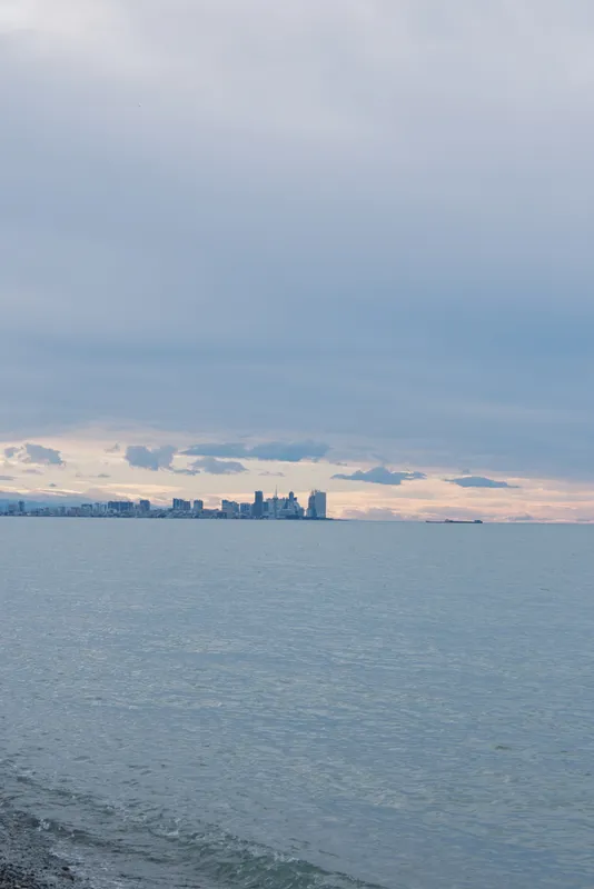 Calm sea stretches to a distant skyline under a muted sky, with a quiet shore and gentle waves composing a peaceful coastal landscape at dusk.