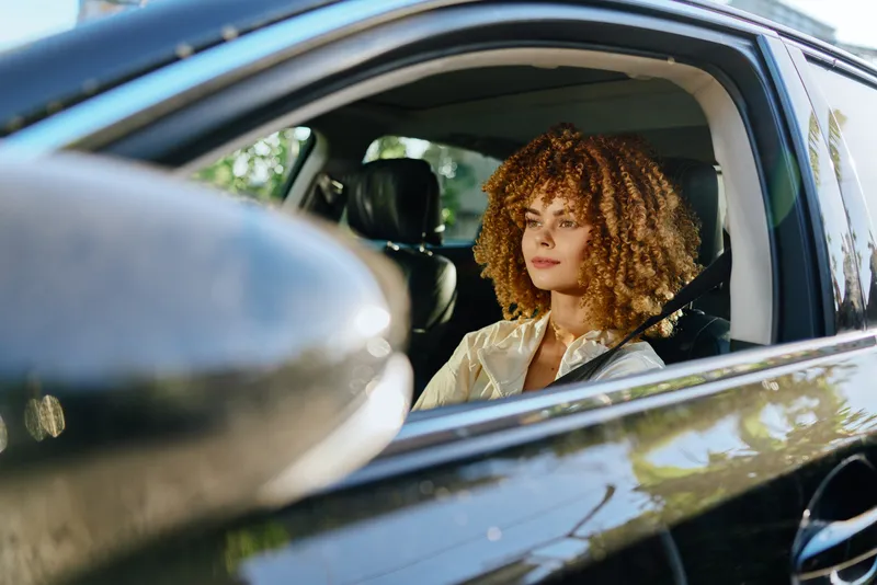 woman with curly hair driving car looking thoughtful, natural light, casual outfit, modern vehicle interior, sunny day atmosphere