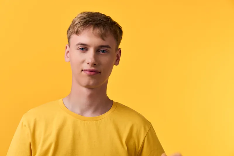 Young man wearing a bright yellow shirt stands against a vibrant yellow backdrop, minimal studio lighting highlights a relaxed pose and confident expression, ideal for fashion, lifestyle, or