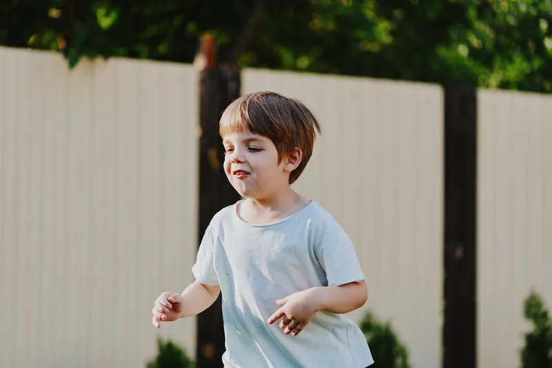 Playful boy enjoying outdoor activities, smiling and running in a garden setting, surrounded by greenery and warm sunlight for a joyful atmosphere.