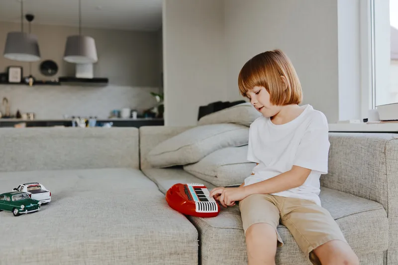 A focused boy playing a toy keyboard in a cozy living room, surrounded by miniature cars, revealing creativity and playfulness in a modern setting.