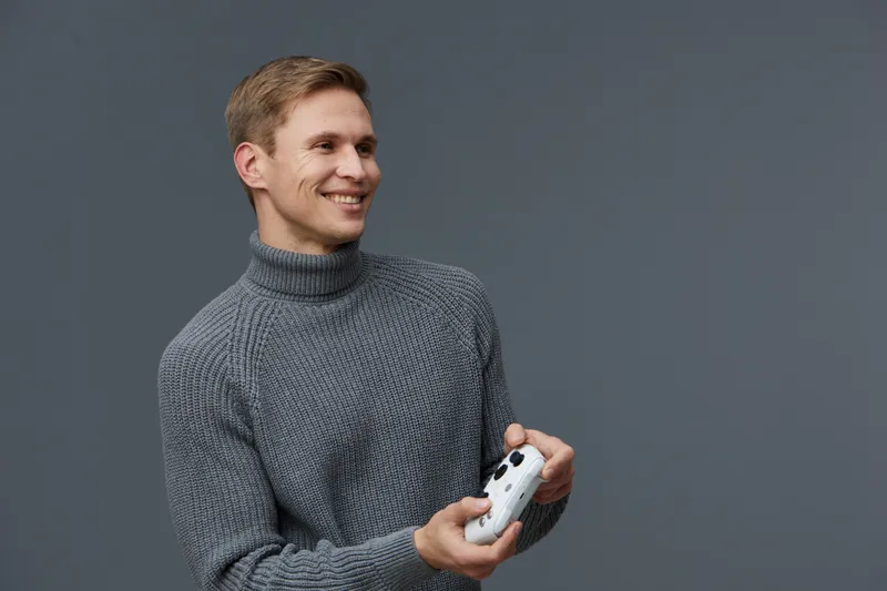 smiling young caucasian man wear gray turtleneck sweater hold game controller play video games isolated on gray background digital detox concept