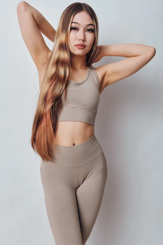Young woman with long hair in sportswear posing with arms raised against white background for fitness and health concept. Slim body, casual style and confident expression indoors.