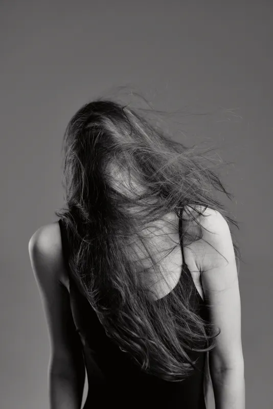 Black and white portrait of a woman with flowing hair in a sleeveless top, capturing motion and emotion in monochrome style.