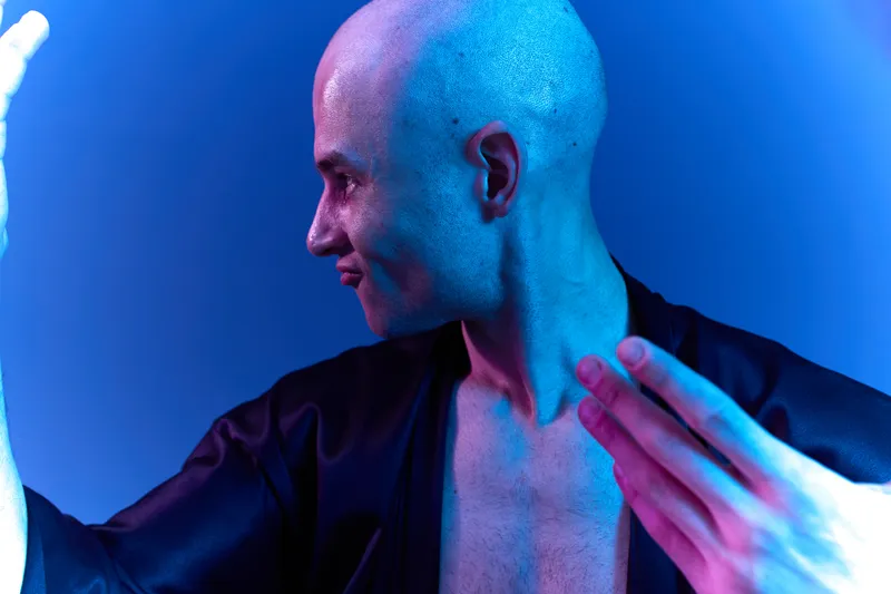 A confident man posing with an expressive gesture, featuring a cool blue lighting scheme. This black and white image emphasizes the unique mood and artistry.