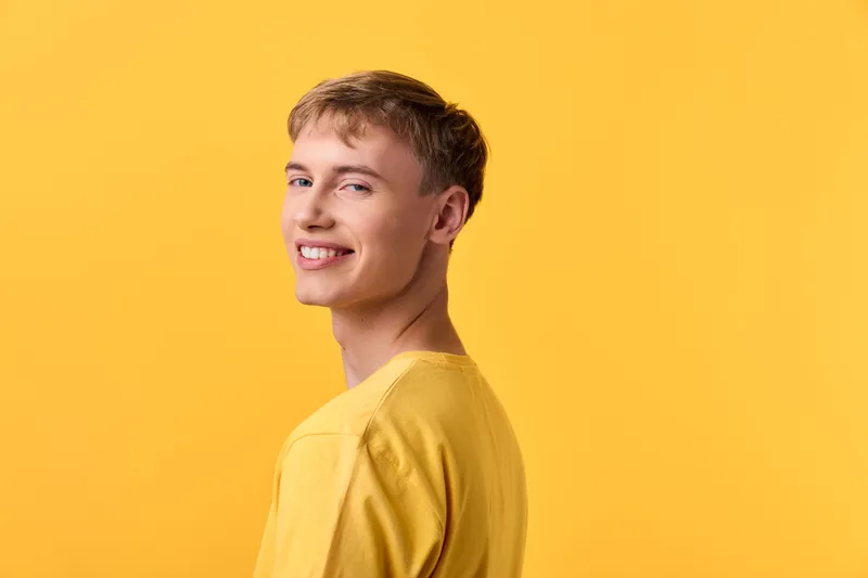 Man smiling in a yellow shirt against a yellow studio background, posed naturally for fashion and lifestyle stock, capturing bright mood, casual style and confident expression.
