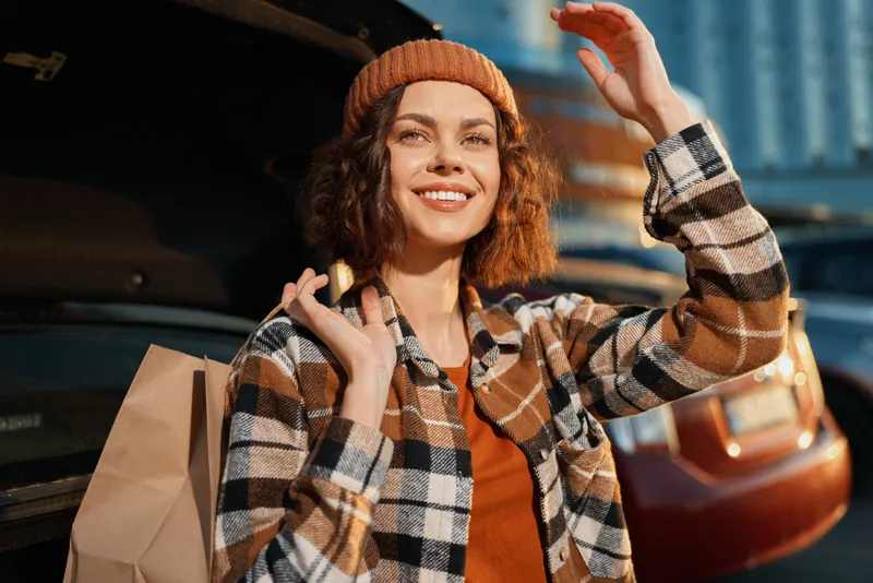 Woman smile shopping car trunk paperbag beanie plaid, candid lifestyle portrait of a happy traveler in golden hour glow, authenticity and emotional storytelling with mindful living vibe.