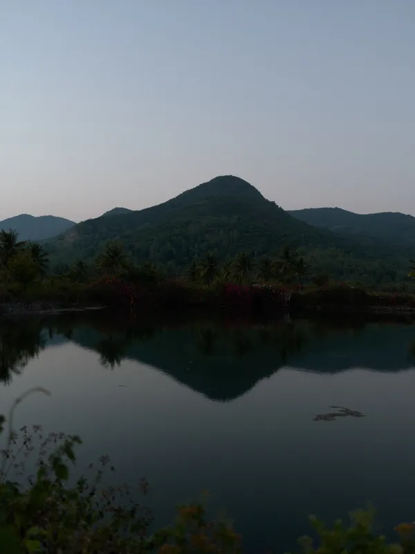 peaceful mountain landscape reflected in calm water during early morning, surrounded by lush greenery and soft natural light, serene outdoor scenery