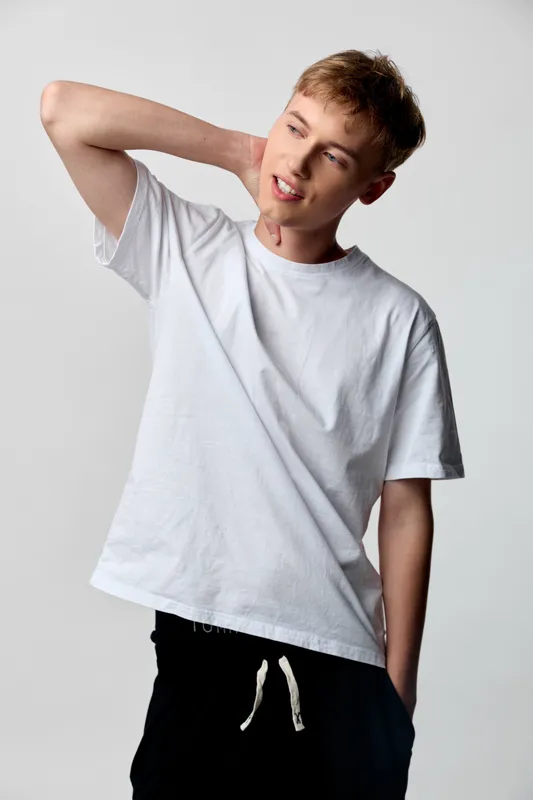 Youthful man in a white tshirt stretches his neck in a casual studio pose, conveying a relaxed mood and simple fitness fashion against a neutral backdrop