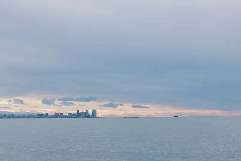 Water and skyline across a calm seascape with clouds and distant city silhouettes, a serene horizonline over blue ocean and peaceful shore at dusk