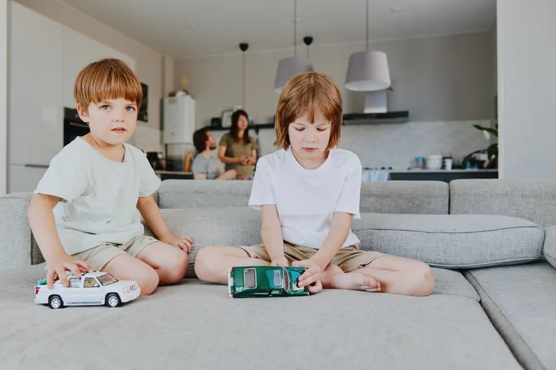 Two young boys playing with toy cars in a cozy living room, showcasing a warm family atmosphere. The scene is inviting and filled with joy and imagination.