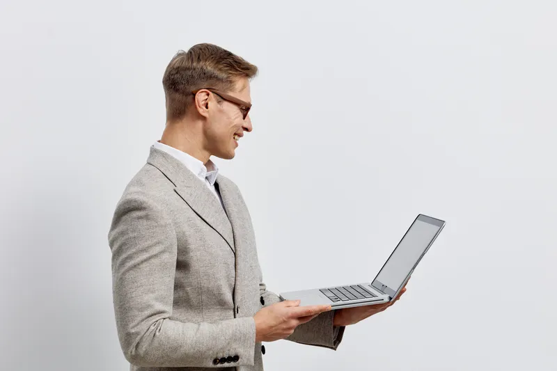 smiling young man with laptop wearing grey suit working digital nomad remote job white background