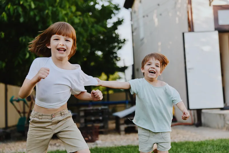 Happy children running outside in a lush garden. Their joyful expressions and energetic movements reflect the pure joy of childhood playtime in a sunny environment.