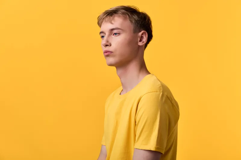 Male wearing a yellow tee stands before a solid yellow backdrop, creating a bold monochrome look with a calm, introspective mood in a clean studio setting, suitable for fashion and lifestyle visuals