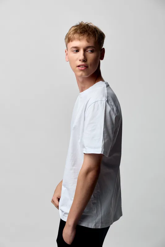 Casual young man in a white t shirt poses in side profile, showcasing relaxed fashion and a minimal studio setting with clean lines, natural attitude and modern style