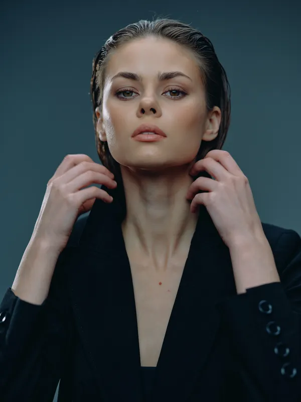 confident woman posing in black blazer with wet hair against dark background, intense gaze, fashion portrait with moody lighting