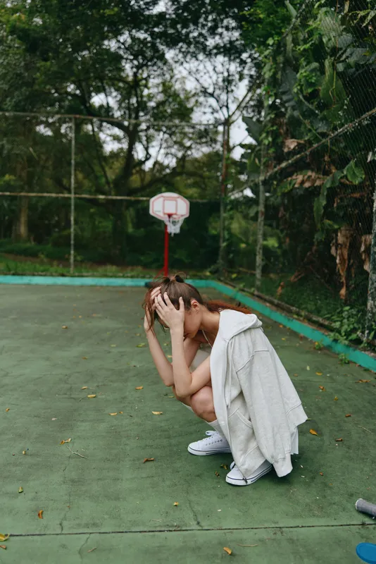 Young woman showing distress on a basketball court, wearing casual sportswear, with a vibrant green background, conveying emotions of frustration and contemplation