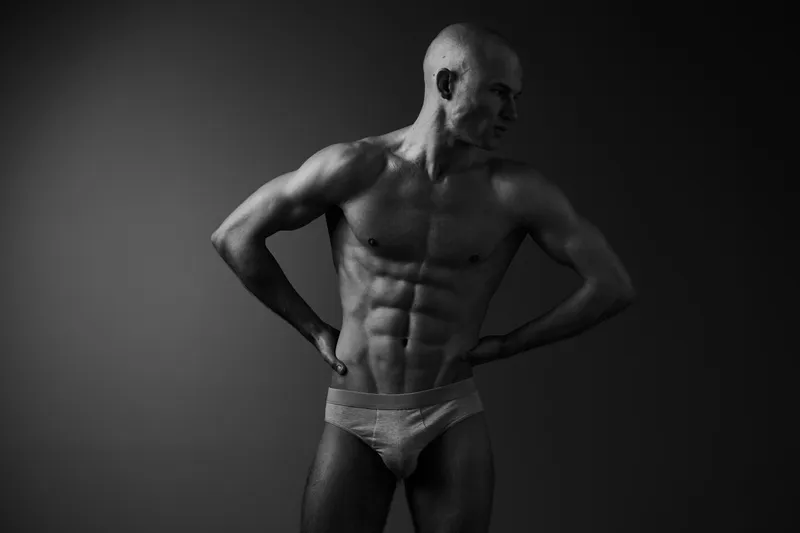 Strong man posing in black and white, showcasing athletic physique and confidence, highlighting muscular definition and artistry in form.