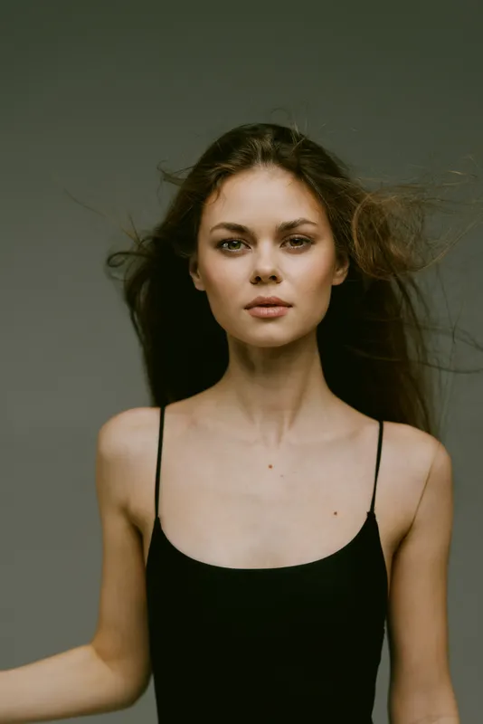 young woman with minimal makeup and loose hair in black dress, natural beauty, calm expression, neutral background