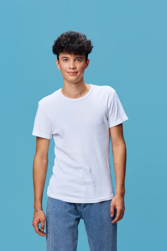 young man wearing a white t-shirt standing against a blue background, casual clothing, relaxed posture, short curly hair, studio portrait