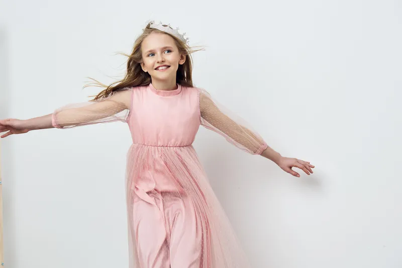 Happy girl in a pink dress with mesh sleeves, dancing joyfully in a bright, minimalistic room, embodying childhood innocence and joy