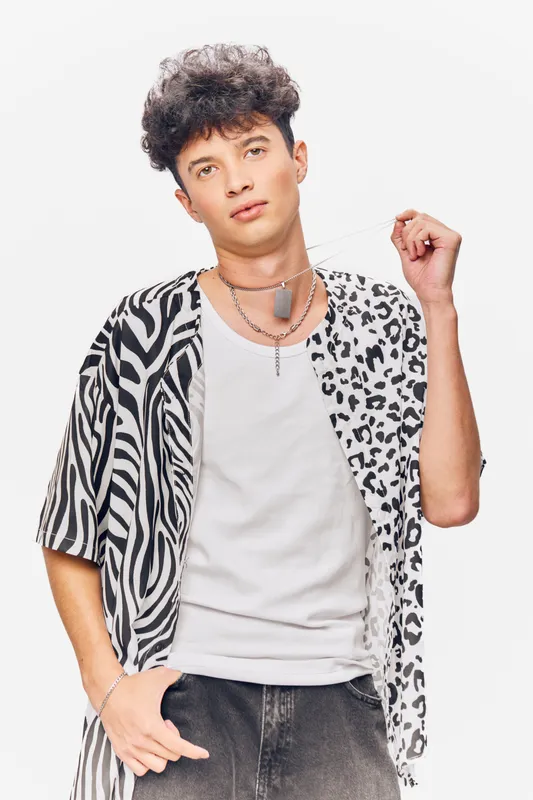 young man wearing a trendy animal print shirt and white tank top posing confidently against a light background with curly hair and casual style