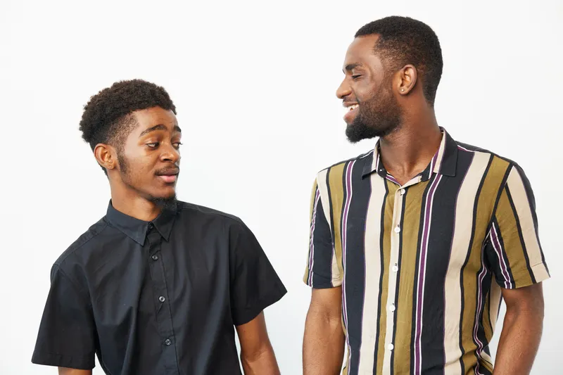 Two smiling African American men engage in a friendly conversation, showcasing joy and camaraderie against a clean, neutral background.
