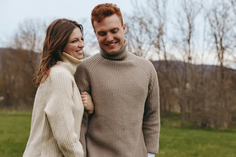 Smiling couple outdoor sweaters happiness together lifestyle fashion cozy romance nature. Soft light captures a candid moment in a park setting, highlighting connection, warmth, and a relaxed, joyful