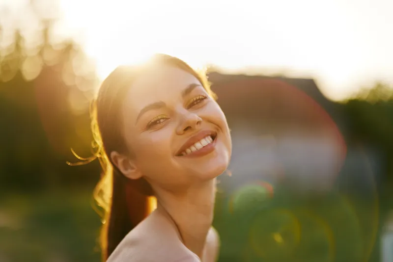 Beautiful young woman smiling in golden hour sunlight with a natural background, embodying joy and positivity, perfect for wellness themes