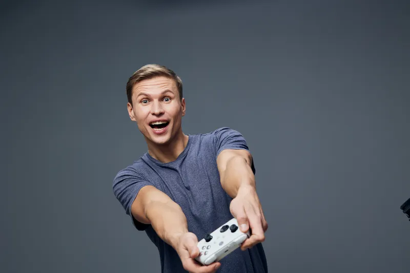 excited young caucasian man holding video game controller wearing casual blue t-shirt isolated on grey background digital detox concept