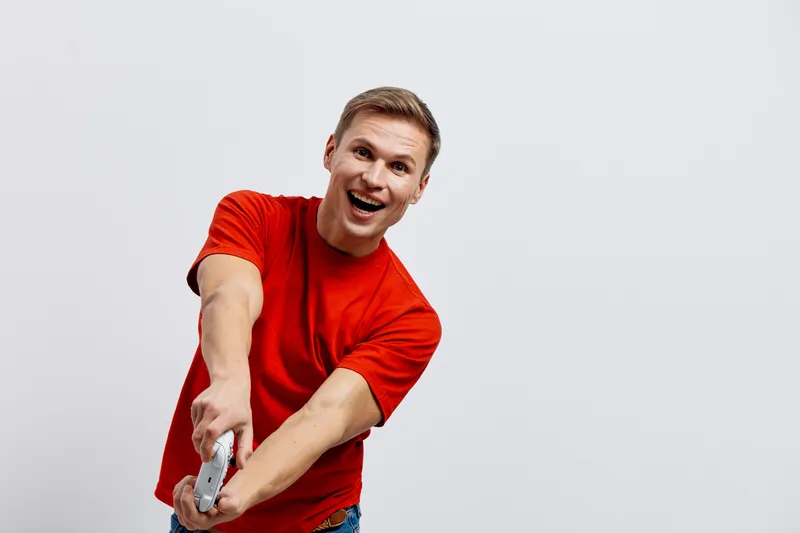 excited young man wearing red t-shirt holding game controller playing video games isolated on white background digital entertainment concept