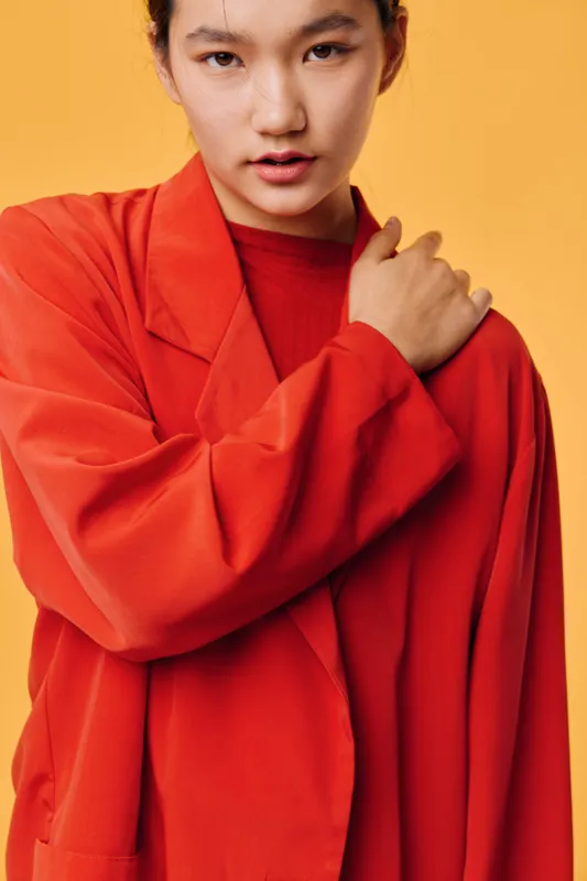 Woman wearing red jacket with serious facial expression, posing in studio with yellow background. Fashion model, portrait and casual style, looking at camera with hand on shoulder.