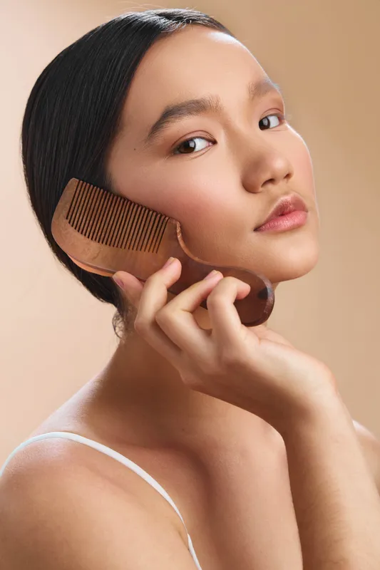 Asian woman portrait is captured in a close up moment as she grooms her hair with a wooden comb, exuding calm poise, soft lighting, and refined beauty routine.