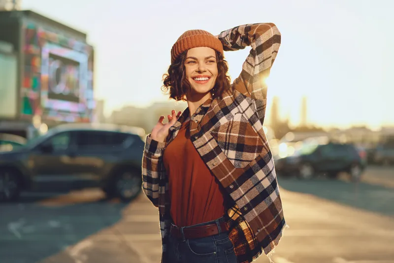 Woman smile urban golden beanie plaid candid lifestyle portrait at golden hour glow, authenticity and emotional storytelling with mindful living vibe and warm backlight in city street.