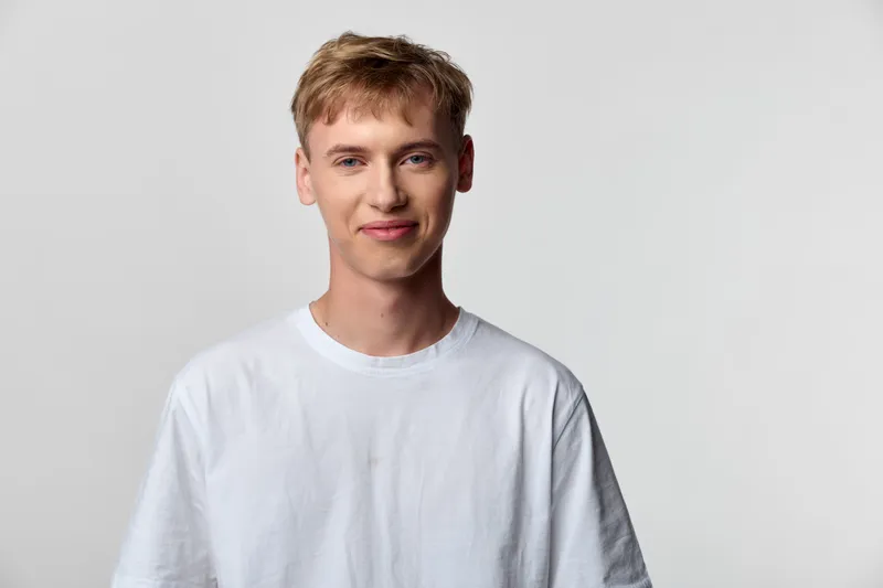 Casual man wearing a white tee stands in a studio with soft lighting and a friendly smile, suitable for lifestyle, fashion, and stock photography contexts
