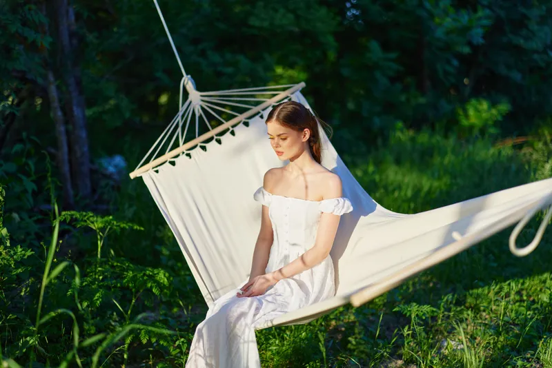 Young woman in white dress sitting on a hammock, surrounded by greenery, exuding tranquility and serenity, perfect for nature themed imagery