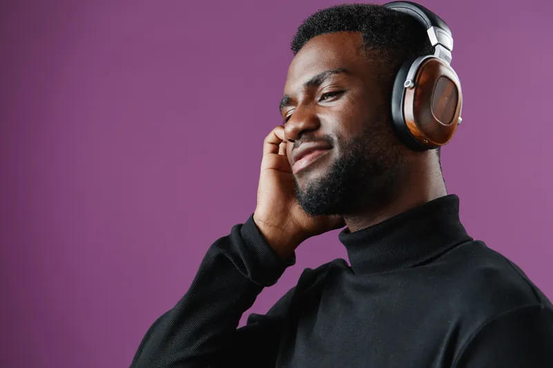Young Black man enjoying music with headphones against a purple background, expressing happiness and relaxation in a modern, stylish setting